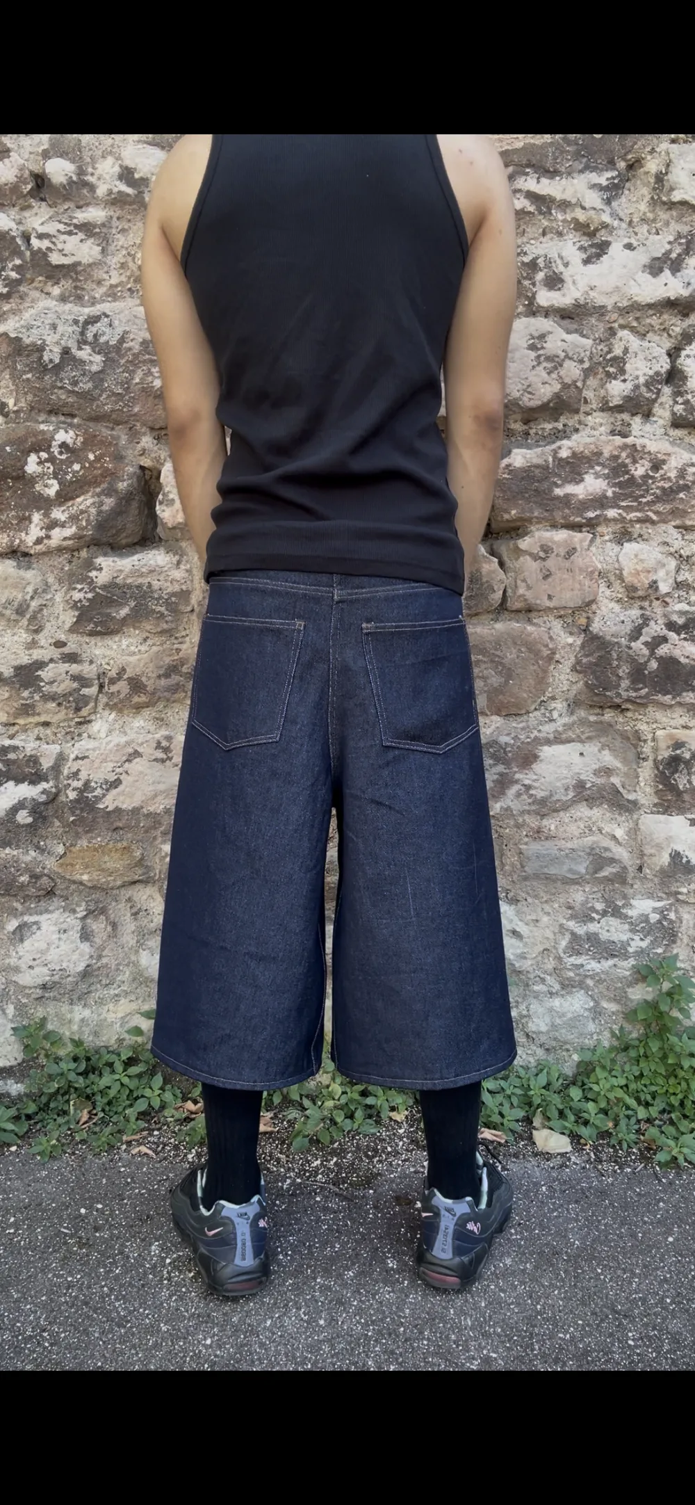 Pantalon en denim brut porté de dos devant un mur en pierre